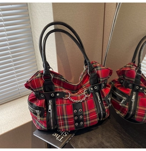 Detail of red and black plaid punk tote bag with metal chains and rivets on a wooden table