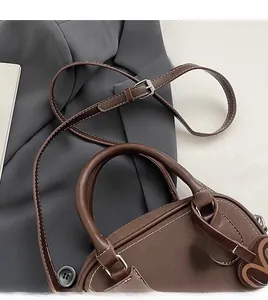 Detail of brown matte Boston bag with white contrast stitching and heart charm on a blazer