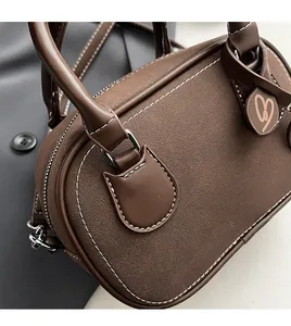 Detail of dark brown leather Boston bag showing white contrast stitching and heart charm