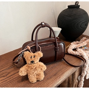 Dettaglio della borsa bowling marrone lucida vintage con ciondolo orsetto su legno