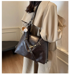 Detalle del bolso de hombro en cuero marrón oscuro con herrajes dorados y dije de béisbol