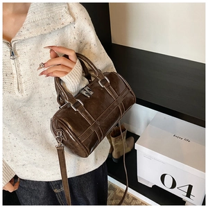 Close-up of brown glossy leather barrel bag with silver hardware held by a model