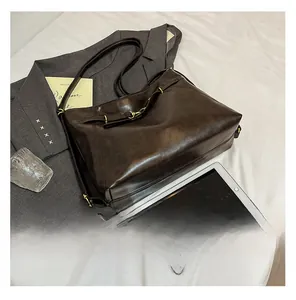 Detail view of large dark brown leather tote bag with gold buckle and long shoulder strap