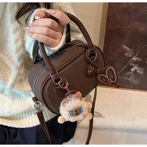 Detail of dark brown Boston bag with contrast stitching and cute plush animal charm