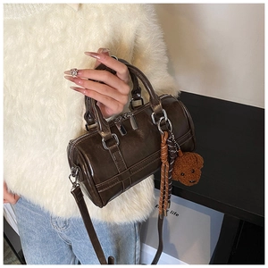 Detail of dark brown mini Boston bag with plush teddy bear charm and strap