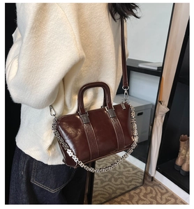 Detailed view of dark brown glossy leather bag with silver chain strap and stitching