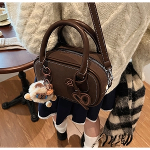 Close-up of brown Boston bag featuring white stitching details and plush bear charm