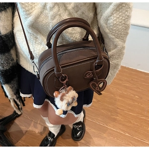 Detail view of dark brown Boston bag with heart charm and plush doll accessory