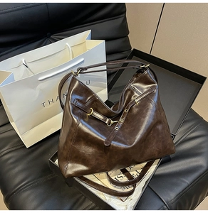 Close-up of deep brown oil wax leather tote bag placed on a black leather sofa