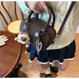 Brown Boston bag detail with white stitching, plush lion charm and heart tag accessory