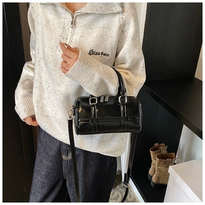 Detail of black patent leather bowling bag with silver hardware on a casual model outfit
