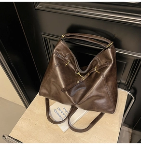 Detail view of the deep brown leather tote bag with gold metal buckle and ring accents