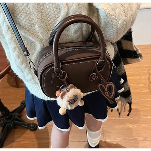 Detail view of brown Boston bag featuring white stitching and cute plush doll pendant