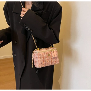 Detail of pink tweed vanity bag with gold chain and floral accents on a black coat