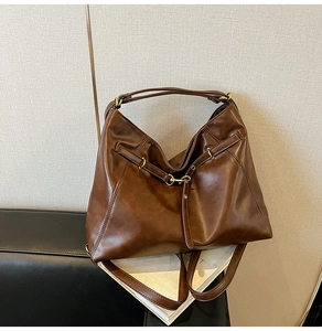 Detail view of large dark brown tote bag with matte leather texture on an indoor bench