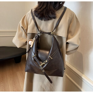 Detalle de la mochila de cuero marrón oscuro con colgante de béisbol y hebillas metálicas