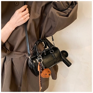 Fashionable black bowling bag with plush puppy pendant styled on a trench coat model