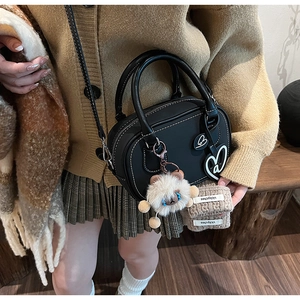 Detail of black Boston bag with white contrast stitching, plush charm, and leather handles