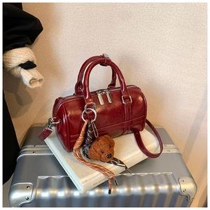 Close-up of deep red bowling bag with plush teddy bear charm on silver luggage background
