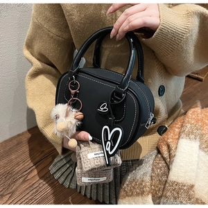 Detail of black leather Boston bag with contrast stitching and yellow plush charm