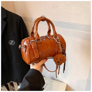 Detail of a brown PU leather Boston bag featuring a plush bear charm and thin strap