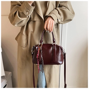 Détail du sac Boston vintage en cuir ciré bordeaux avec pompon tressé et bandoulière