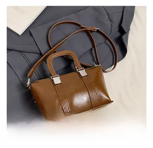 Detail of caramel leather trapezoid bag with silver metal buckles on grey suit backdrop