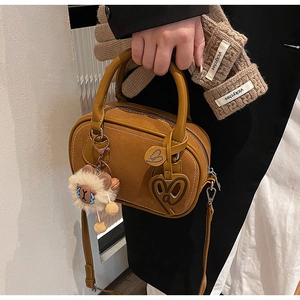 Close-up of brown suede Boston bag with plush lion charm and metal heart tag detail