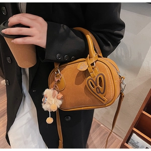 Detail of the brown boston bag showing matte texture with heart charm and plush pendant