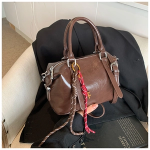 Détail du sac Boston en cuir ciré marron foncé avec corde décorative sur un blazer