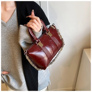 Close-up of burgundy glossy leather handbag with silver G-link chain and decorative stripes