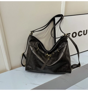 Detail of vintage black leather tote bag featuring retro bronze metal buckles and loops