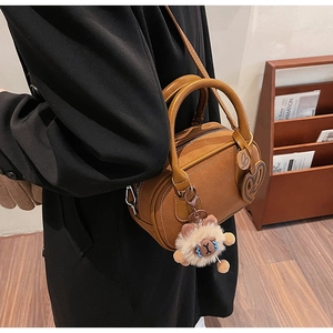 Close-up of brown Boston bag with teddy bear charm and heart detail on model