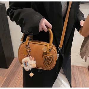 Close-up of caramel suede Boston bag with plush doll charm and heart leather tag