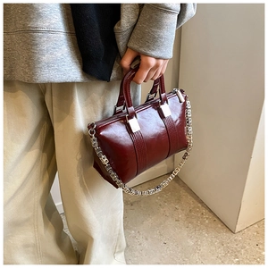 Detail of burgundy glossy crossbody bag with thick silver chain strap and top handles