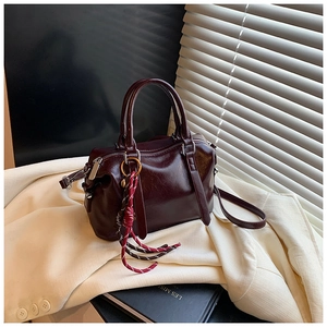 Détail du sac Boston en cuir ciré marron avec pendentif tissé posé sur une veste