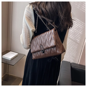 Brown quilted crossbody bag with V-shaped stitching and chain strap worn by model