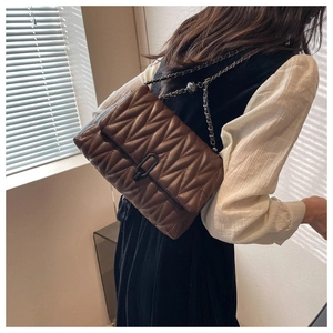Brown quilted crossbody bag with V-shaped stitching and black chain strap shown on model