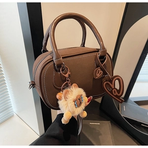 Detail of dark brown Boston bag featuring white contrast stitching and plush lion charm