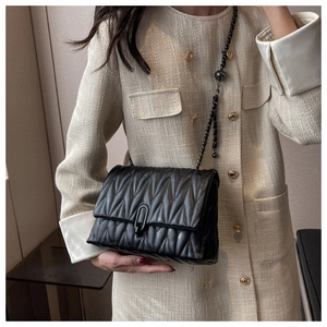 Detail of black quilted leather shoulder bag with matte metal chain and lock