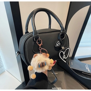 Detail of black leather Boston bag with white stitching and cute brown bear charm