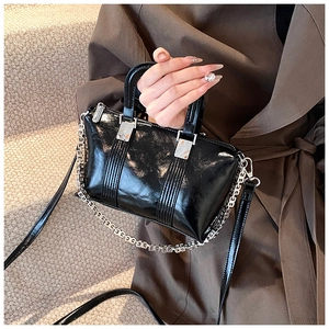 Close-up of black patent leather crossbody bag with decorative silver chain and pleats
