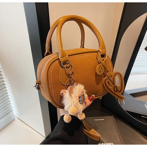 Detail of tan Boston bag with plush lamb pendant and heart tag on smooth matte leather