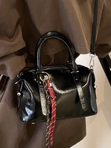 Sac Boston noir brillant en cuir ciré avec pendentif sur un modèle portant un trench