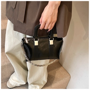 Detail of a black patent leather handbag with a signature G-shaped metal chain strap