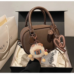 Detail of a dark brown leather Boston bag in a luxury gift box with a plush bear charm