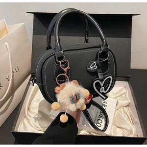 Detail of black Boston bag with white stitching and plush charm in a luxury gift box