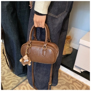 Détail du sac Boston marron rétro avec logo embossé et breloque en peluche mignonne