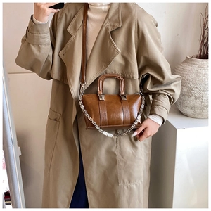 Deep brown vintage leather handbag with silver chain and adjustable strap on a trench coat