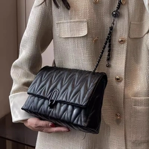 Sac bandoulière noir matelassé avec chaîne en métal et boucle en U porté par un mannequin